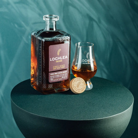 Lochlea Dark Briar Lowlands Single Malt Scotch Whiskyflasche mit halb gefülltem Gkas auf einem runden Tisch
