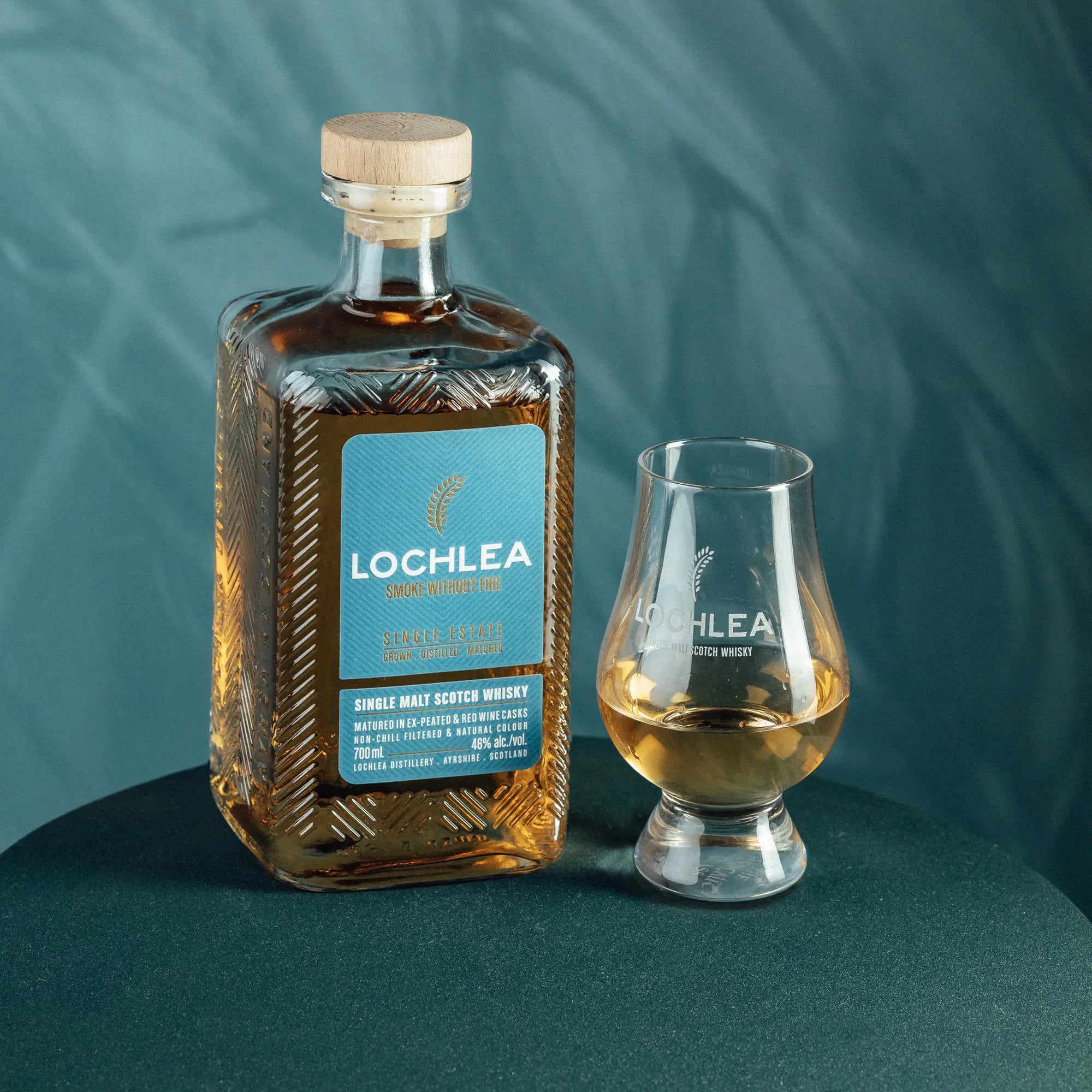 Lochlea Smoke without Fire Lowland Single Malt Scotch Whiskyflasche und halb gefülltes Glas auf einem runden Tisch