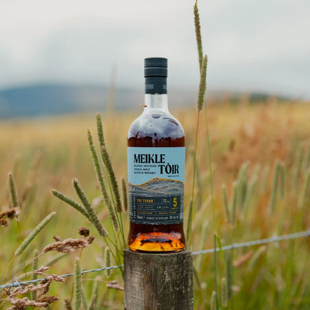 Meikle Tòir The Turbo 5 Jahre 2025 Edition Single Malt Whisky auf einem Holzpfahl vor einem Gerstenfeld